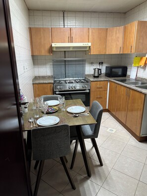 A compact kitchen with wooden cabinets, a gas stove, a microwave, and a sink. - Splendid 2BHK in Al Khan, Sharjah near Dubai/Sharjah border with balcony (Sharjah)