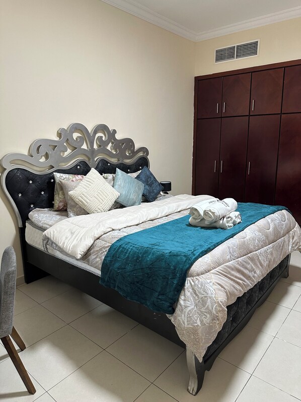 A neatly made bed with a dark headboard, a teal blanket, and multiple pillows. - Splendid 2BHK in Al Khan, Sharjah near Dubai/Sharjah border with balcony (Sharjah)
