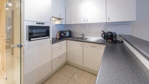 Uma cozinha moderna com armários brancos, forno embutido, micro-ondas, máquina de café e pia.