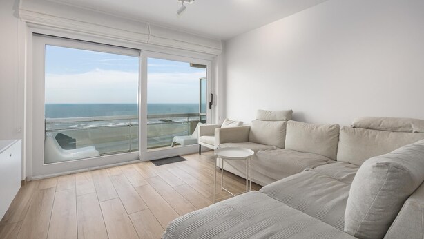 Ein modernes Wohnzimmer mit einem großen Schiebeglasfenster, das auf einen Balkon mit Meerblick führt.