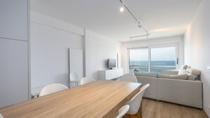 Ein modernes Interieur mit einem Holztisch, weißen Stühlen, einer Couch und einem Fernseher auf einem weißen Schrank.