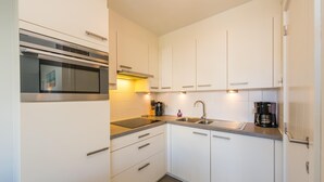 Una cuina moderna amb armaris blancs, un forn d'acer inoxidable, un rentaplat i una cafetera.
