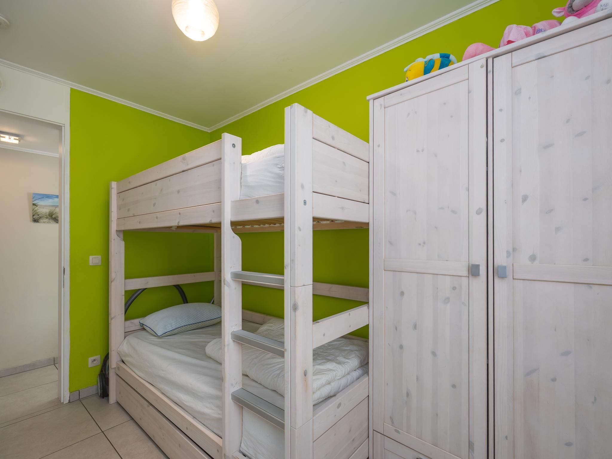 Une chambre avec un lit superposé, un mur vert et des meubles blancs.