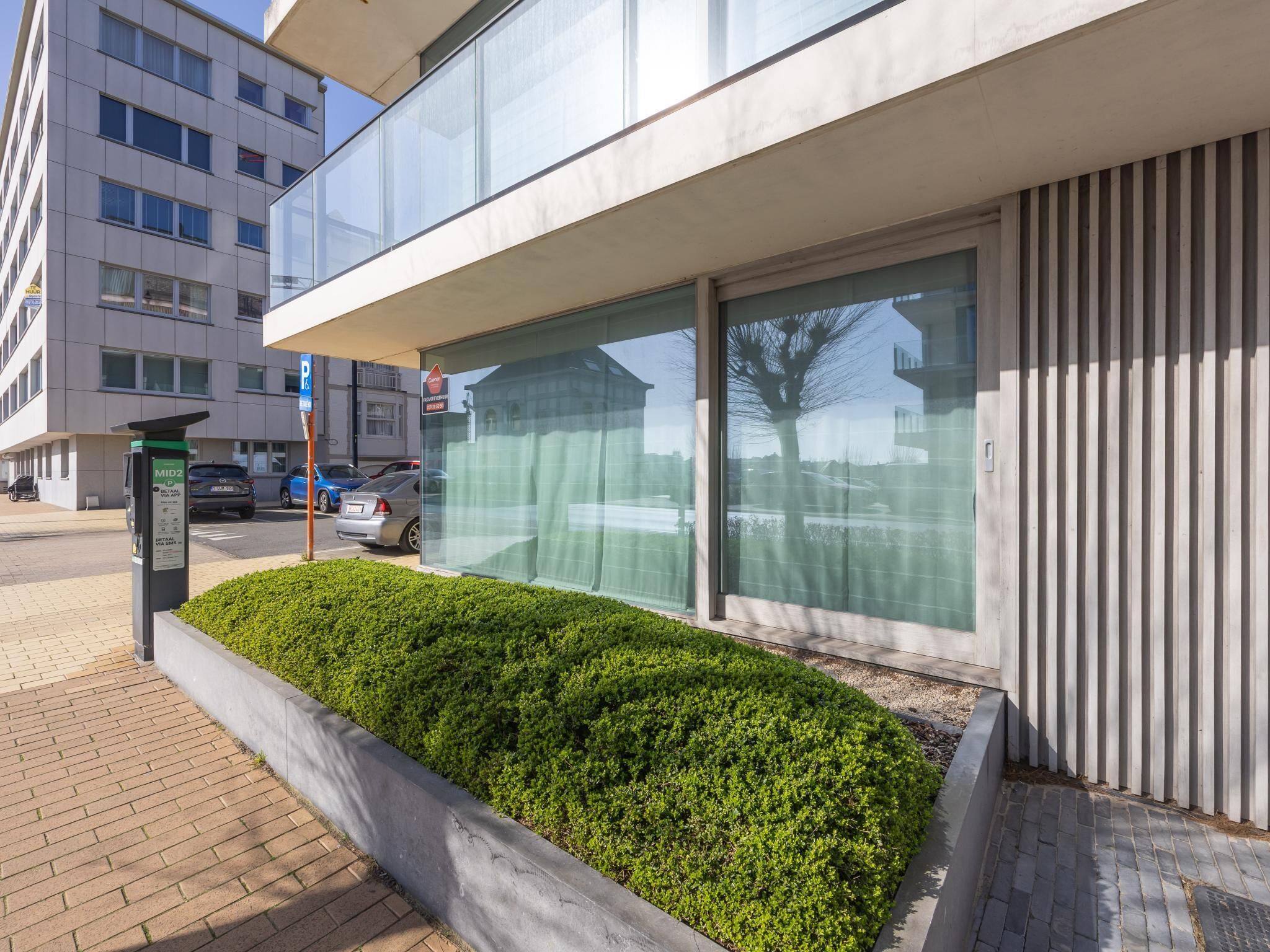 Un edificio moderno con un'ampia vetrata, un segnale di parcheggio e un'area verde con arbusti.