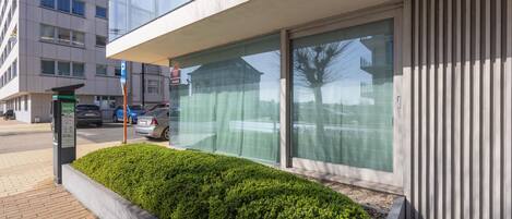 Un edificio moderno con un'ampia vetrata, un segnale di parcheggio e un'area verde con arbusti.
