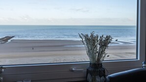 A view of the beach through a window, with a vase of dried flowers on the windowsill. - Cosy studio with sleeping area and sea view (Middelkerke)