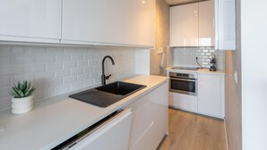 A modern kitchen with white cabinetry, a black sink, and a built-in oven. - Cosy studio with sleeping area and sea view (Middelkerke)