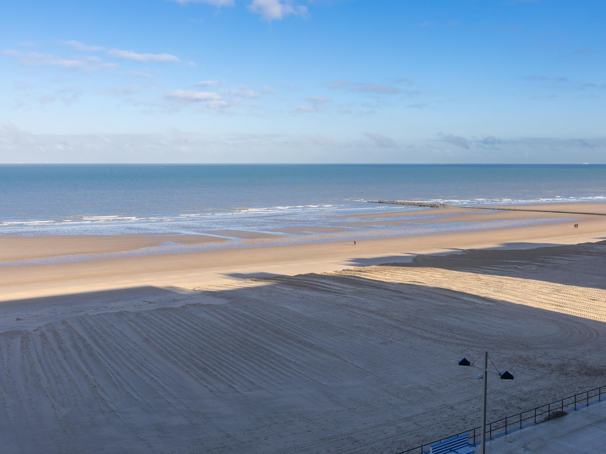Ein Strand mit klarem Himmel, sandigem Ufer und einigen Spaziergängern.