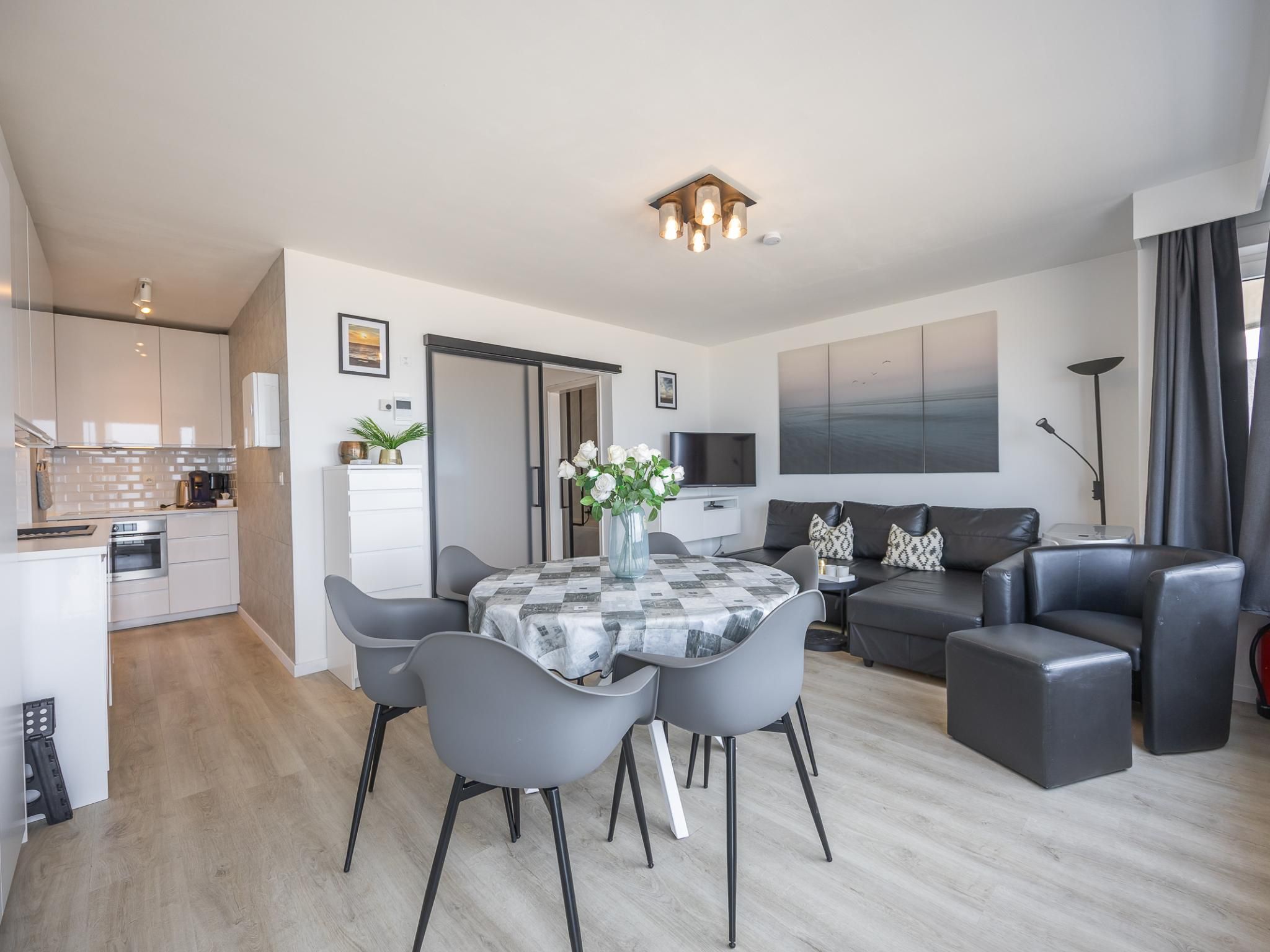 A modern apartment with a dining area, kitchen, living room, and a large window.