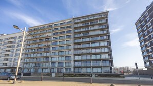 Un edificio residencial de varios pisos con fachada uniforme, balcones y una zona pavimentada al frente.