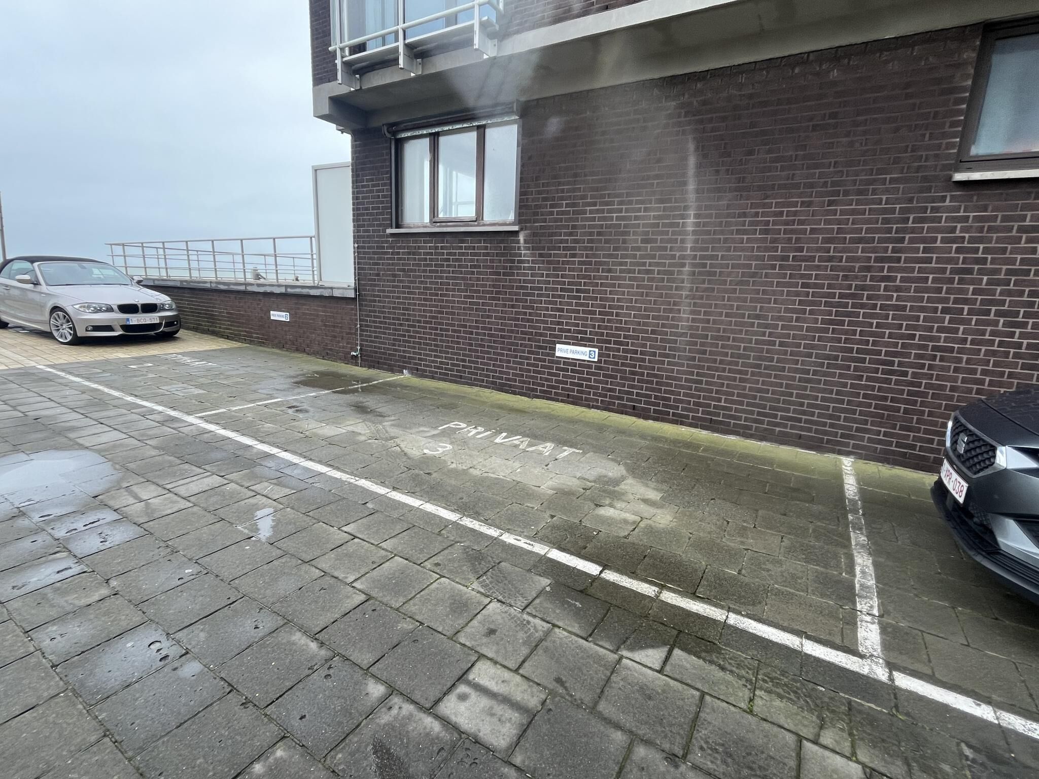 En parkeringsplats med en byggnad av tegel, en bil och en skylt som visar att det är privat parkering.