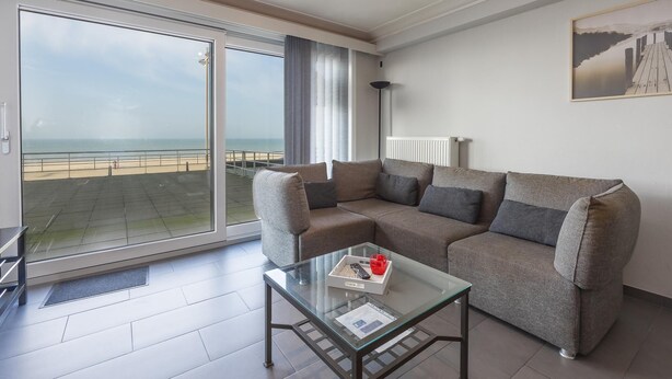 Una sala de estar moderna con un amplio ventanal corredera que da a un balcón con vistas a la playa.