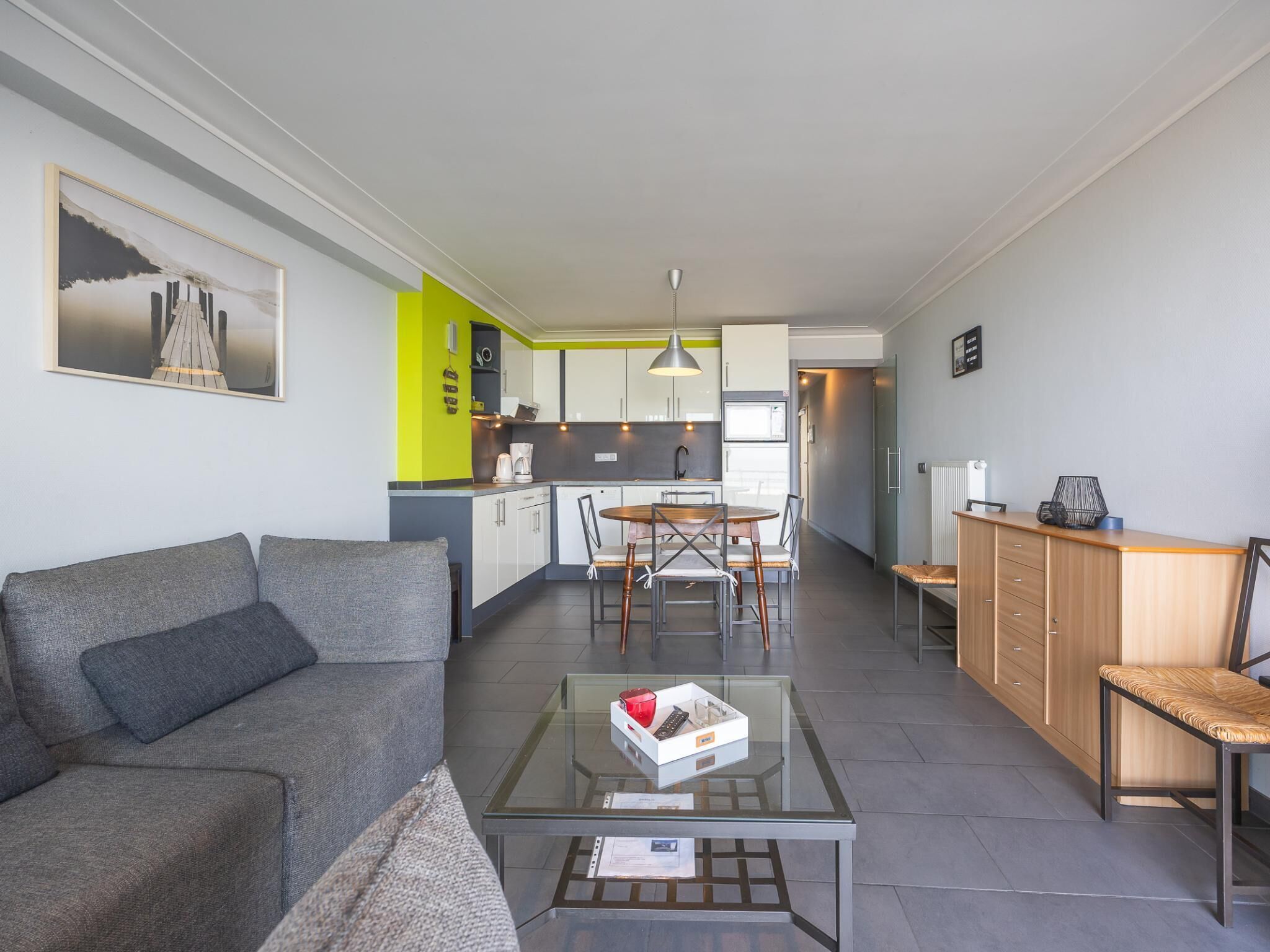 Una sala de estar moderna con una mesa de centro de vidrio, un sofá gris y una zona de comedor con una mesa y sillas de madera.