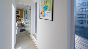 Ein modernes Interieur mit einem gerahmten abstrakten Gemälde, einer Glastür, die in einen Essbereich führt, und Blick auf ein Gebäude im Freien.