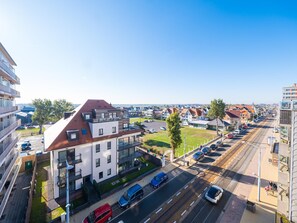 A modern building with a sloped roof, large windows, and a parking area with cars. - Exclusive penthouse with 2 sunny terraces (Middelkerke)