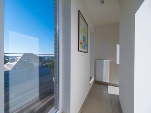 A narrow hallway with a window overlooking a cityscape, a radiator, and a framed abstract painting on the wall.