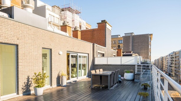Eine Dachterrasse mit Holzdeck, Sitzgelegenheiten im Freien und Topfpflanzen.