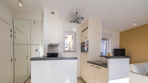 Eine moderne Küche mit weißen Schränken, einem eingebauten Backofen und einem Essbereich mit einem weißen Sofa und einem Fernseher.