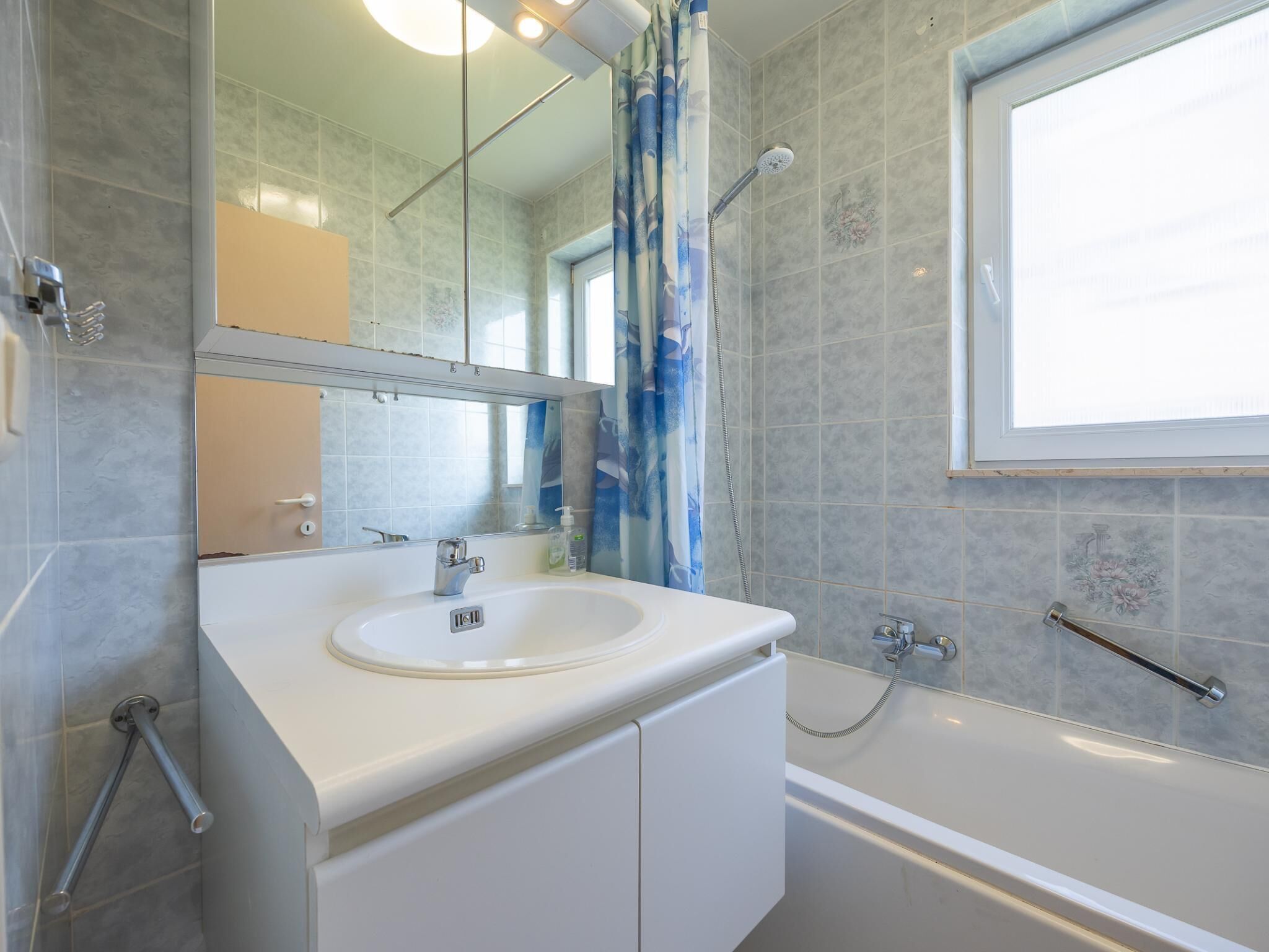 Een moderne badkamer met een witte wastafel, een spiegel, een douche en een raam.