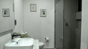 Ein modernes Badezimmer mit einem weißen Waschbecken, einer Toilette und einer Dusche. An der Wand befinden sich Bilder in Rahmen.