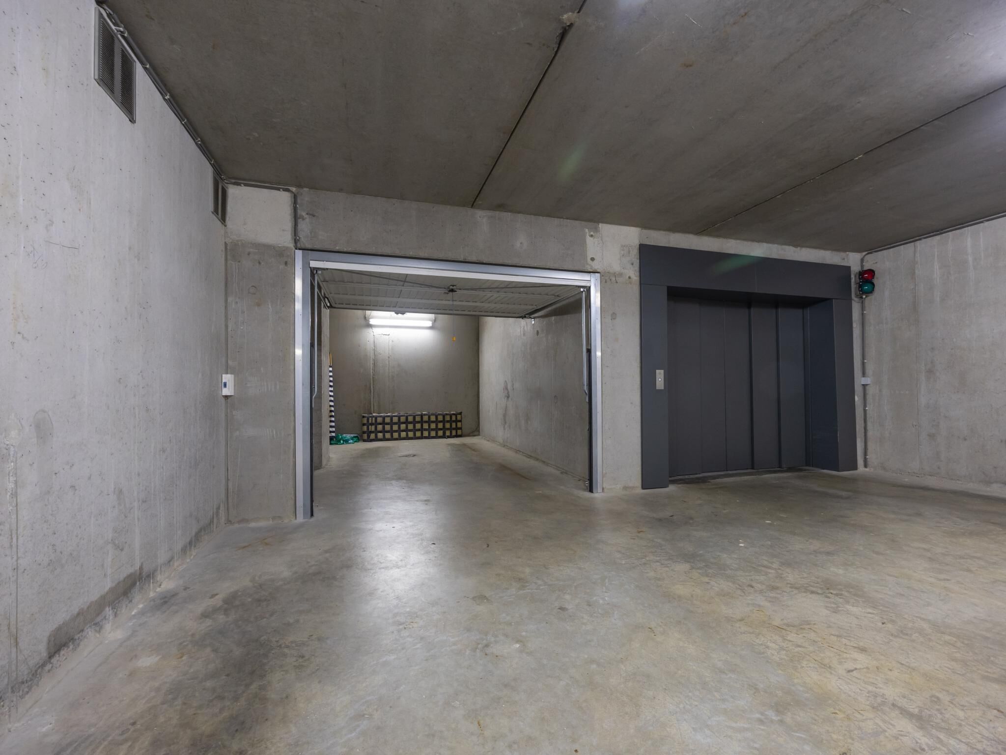 Um corredor de concreto com uma porta que dá para uma área de estacionamento e um elevador.