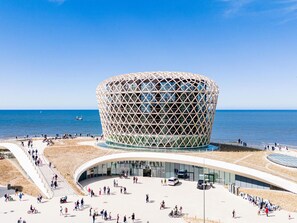 A modern architectural building with a unique geometric design, situated by a waterfront with a promenade and people walking around. - Apartment on the 6th floor with sea view (Middelkerke)