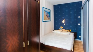A bedroom with a wooden wardrobe, a bed with white bedding, a wall-mounted nightlight, and a star-patterned wall. - Apartment on the 6th floor with sea view (Middelkerke)