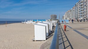 A beachside promenade with a row of white beach huts, a modern building with a unique spherical structure, and a tall residential building with balconies. - Stunning apartment with phenomenal sea view (Middelkerke)
