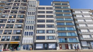 A modern multi-story building with a mix of residential and commercial spaces, featuring balconies, large windows, and a visible storefront. - Stunning apartment with phenomenal sea view (Middelkerke)
