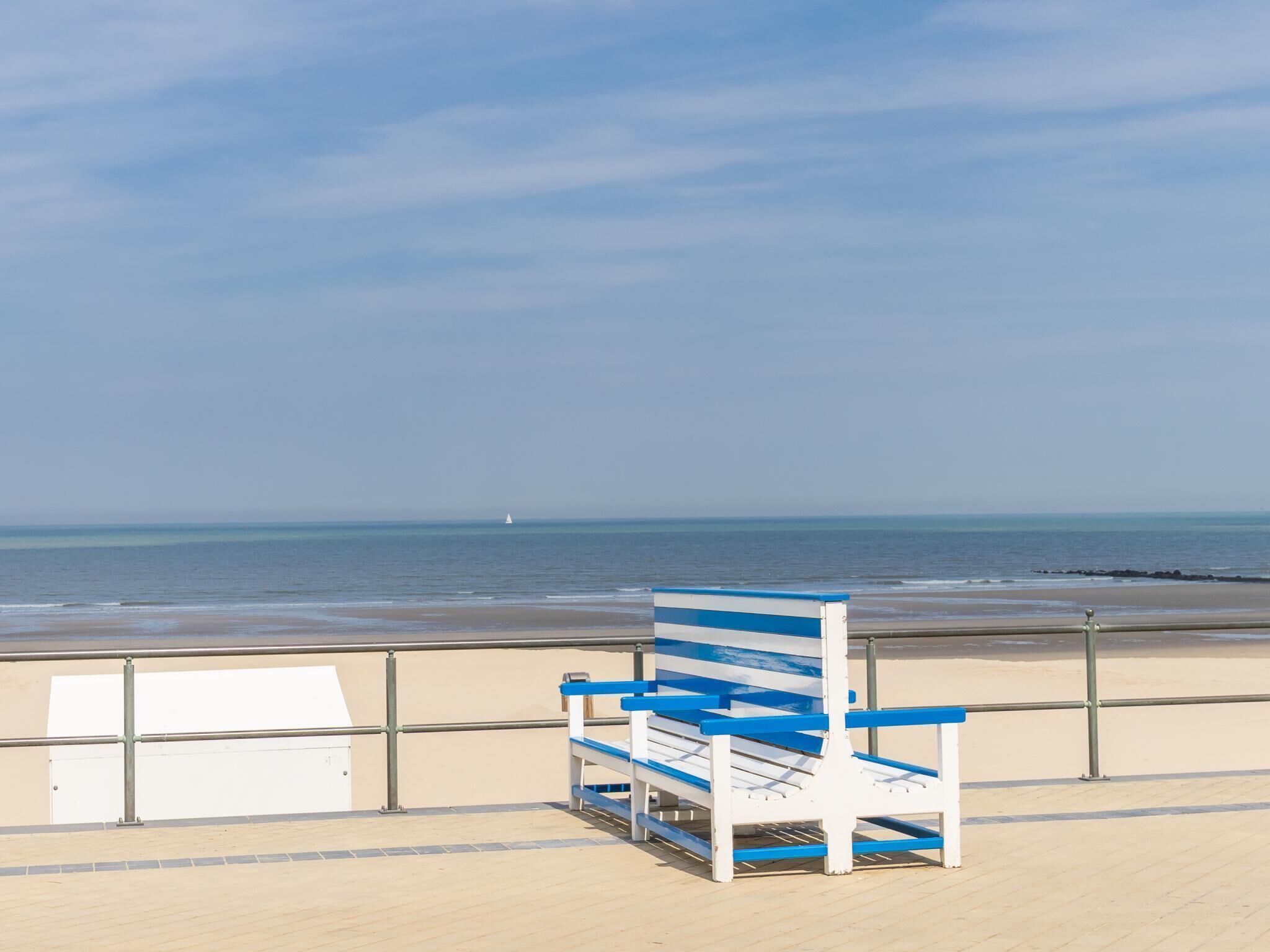 A beach chair with a blue and white design, positioned on a wooden deck overlooking the ocean.