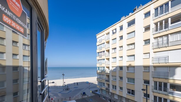 Vista da un balcone su una spiaggia, con un'area parcheggio e un edificio a più piani con balconi.