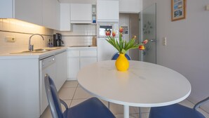 Una cucina moderna con mobili bianchi, un lavello e un fornello. Si nota un tavolo da pranzo con sedie e un vaso di fiori.
