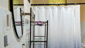 A bathroom with a white sink, a mirror, a shelf with toiletries, and a shower curtain.