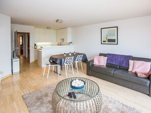 Een moderne woonkamer met een glazen salontafel, een bank en een eethoek met stoelen.
