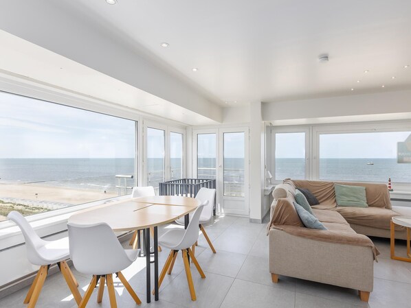 Una habitación amplia con una gran mesa y sillas, un sofá, y vistas al mar.