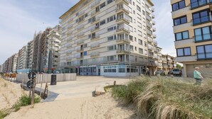 Un edificio a più piani con balconi, una spiaggia sabbiosa di fronte e un cielo sereno.