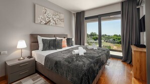 A modern bedroom with a large bed, bedside tables, a nightstand, a wall-mounted TV, and a large window with curtains. - Villa Rose (100541-K1) - Porec (Porec)
