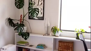 Een slaapkamer met een bed, een wit bureau, een boekenkast, een raam en een kamerplant.