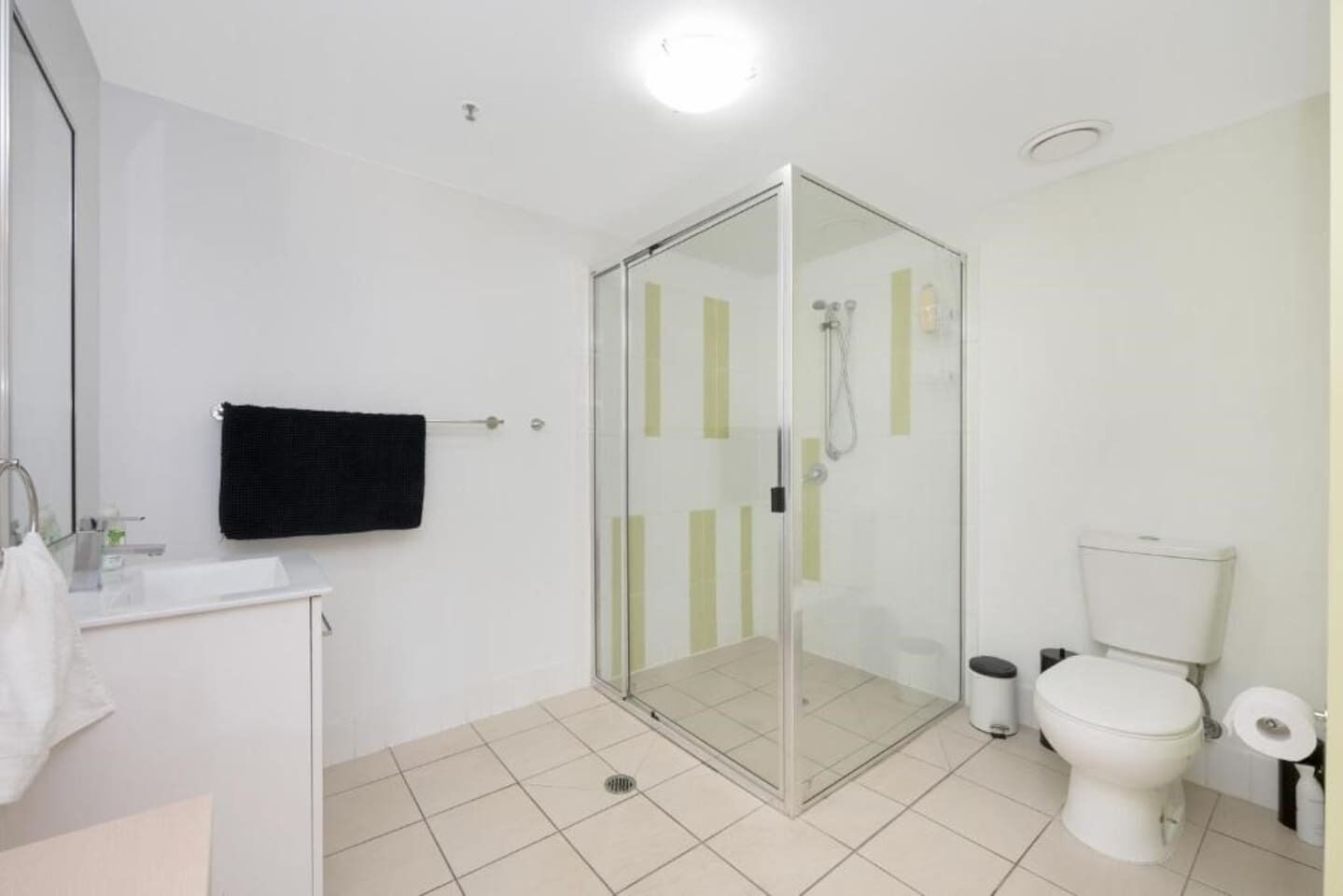 A bathroom with a glass-enclosed shower, a white toilet, and a sink with a towel hanging on the wall.