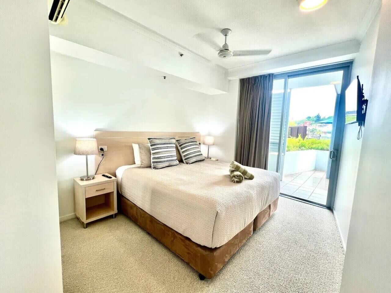 Une chambre d’hôtel avec un lit, une table de chevet, une lampe et une vue sur l’extérieur, visible à travers une porte vitrée.