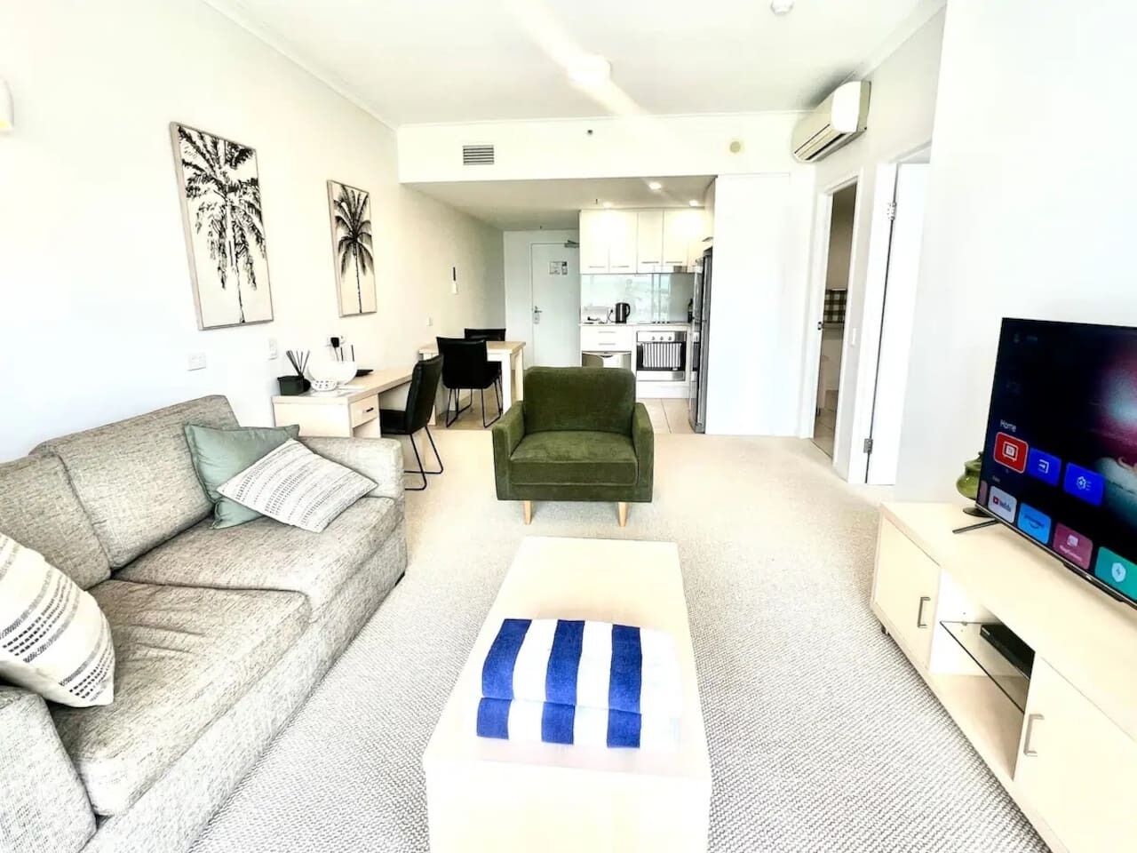 A modern living room with a sofa, a coffee table, a television, and a kitchen in the background.