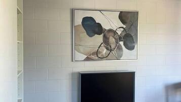 A room with a white brick wall, a flat-screen TV on a wooden stand, and a ceiling fan.