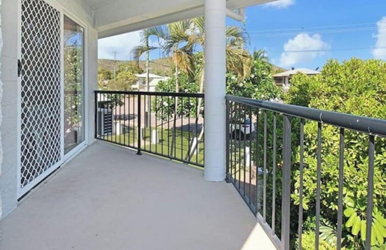 A balcony with a metal railing, a white lattice screen, and a view of greenery and buildings in the background.