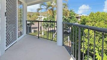 A balcony with a metal railing, a white lattice screen, and a view of greenery and buildings in the background.