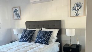 A bedroom with a bed, two bedside tables, a ceiling fan, and a wall-mounted air conditioner. - 1 Bed Apartment on Henry (West End)
