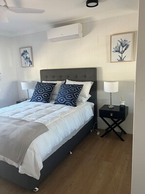 A bedroom with a bed, two bedside tables, a ceiling fan, and a wall-mounted air conditioner. - 1 Bed Apartment on Henry (West End)