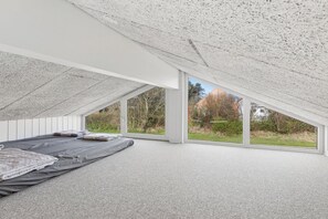 A bedroom with a sloped ceiling, large windows, and a bed with pillows.