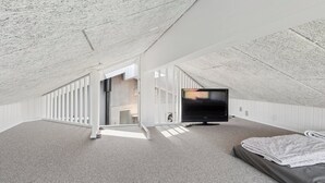 A high-ceilinged attic bedroom with a large flat-screen TV, a bed, and a staircase leading to an upper level. - Super nice holiday home with whirlpool (Højslev)