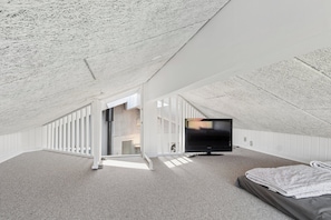 Een zolderkamer met hoge plafonds, een grote flatscreen televisie, een bed en een trap naar een hoger gelegen niveau.