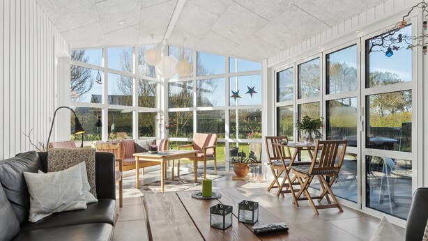 A sunroom with large windows, a wooden table, a sofa, and chairs. - Super nice holiday home with whirlpool (Højslev)